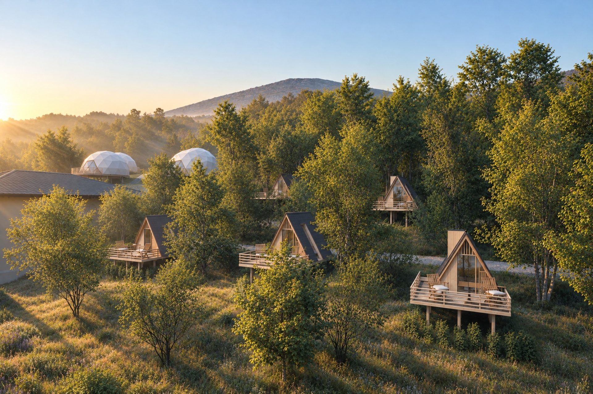 A-frame cabins on stilts among the trees in early morning sun, two geodesic domes and the mountain behind